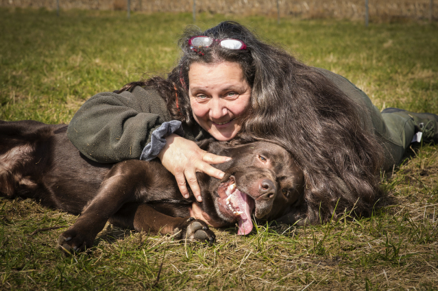 Manuela Schoone liegt mit ihrem Hund auf einer Wiese und schaut zufrieden in die Kamera